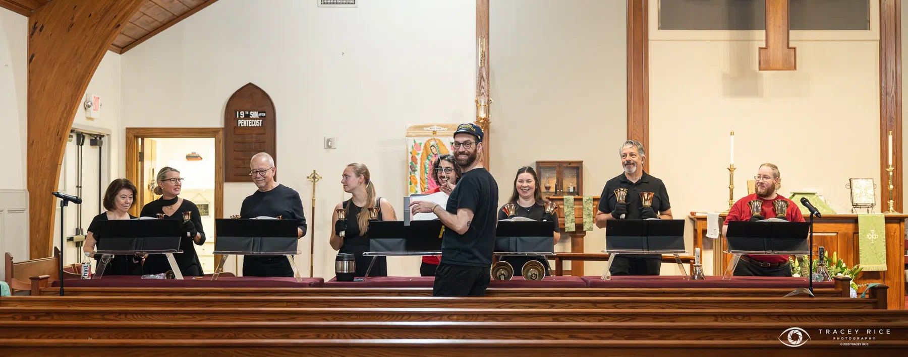 The handbell choir at their tables across the front of the church during rehearsal.