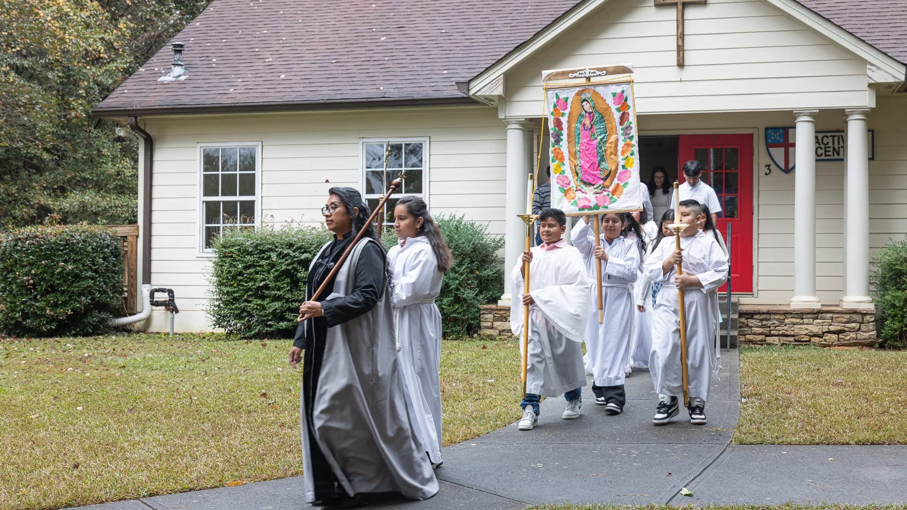 A procession leaving the church carrying a banner of Our Lady of Guadalupe.