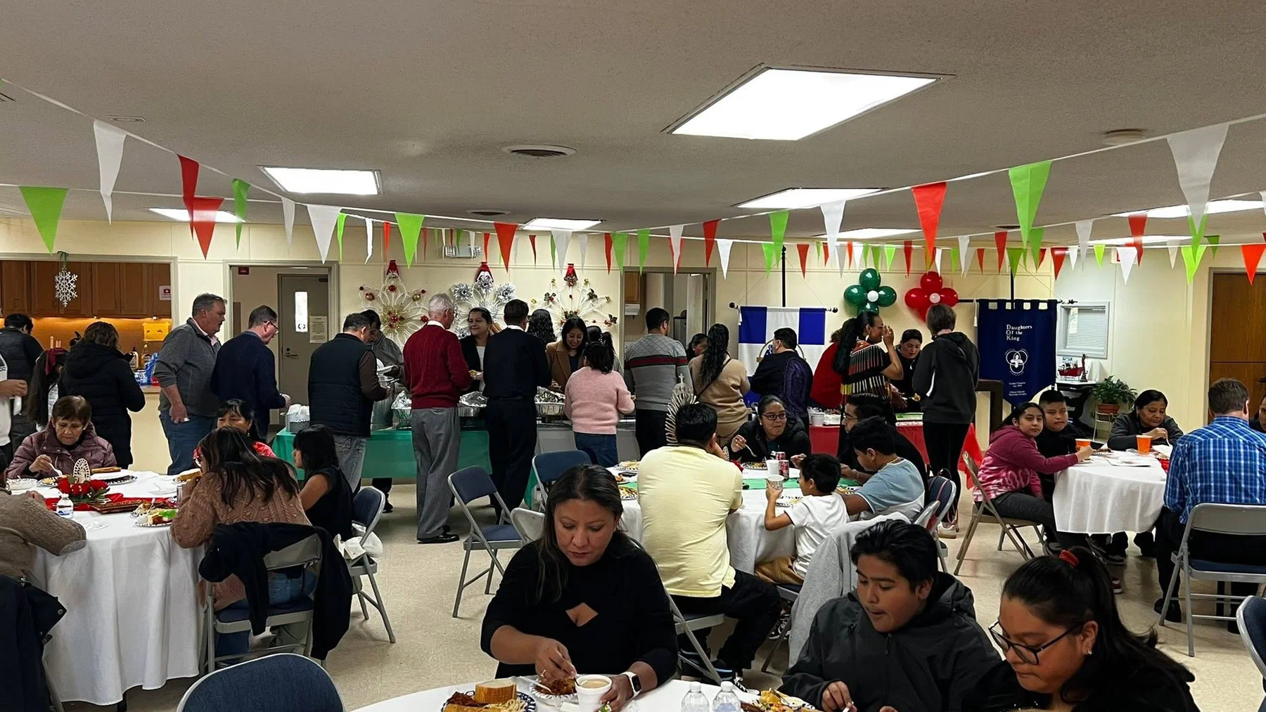 A parish hall full of people sharing a meal beneath red, white and green bunting.