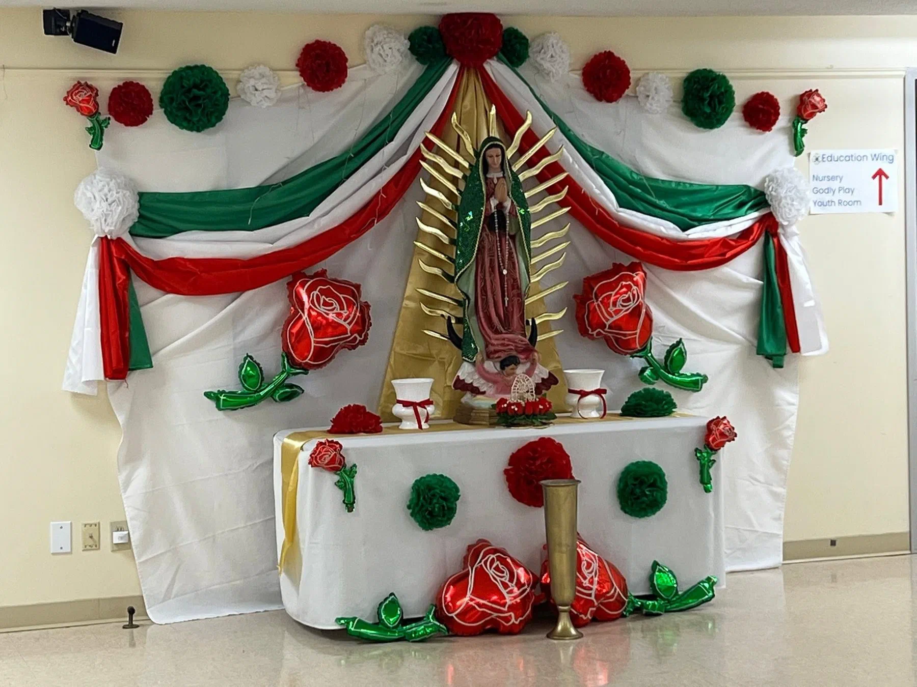 An altar decorated in red, white and green with an image of Our Lady of Guadalupe.